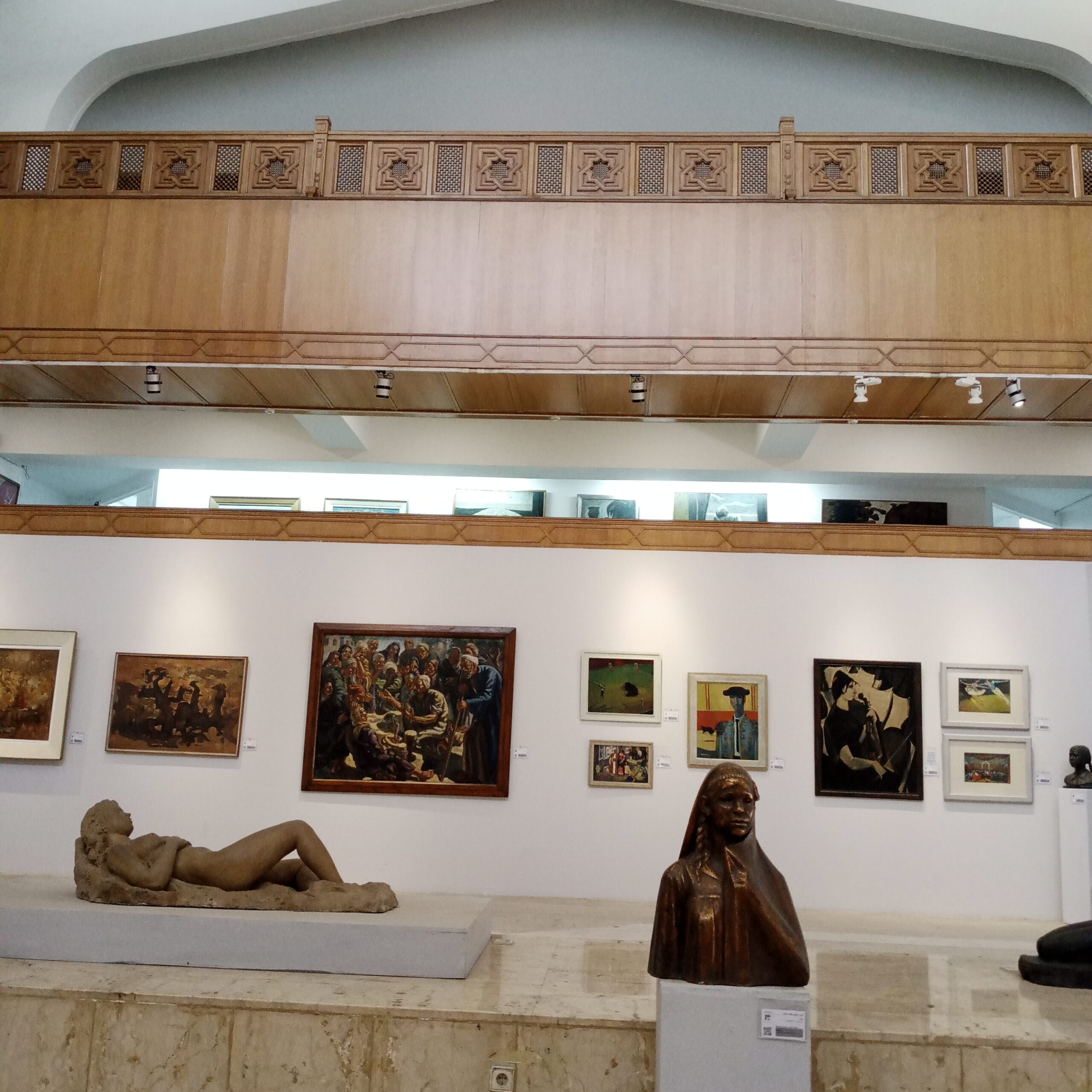قاعة عرض فني في متحف الفن المصري الحجيث القاهرة تضم لوحات مصرية حديثة ومنحوتات كلاسيكية، بإضاءة سقفية وبلكونة خشبية مزخرفة.