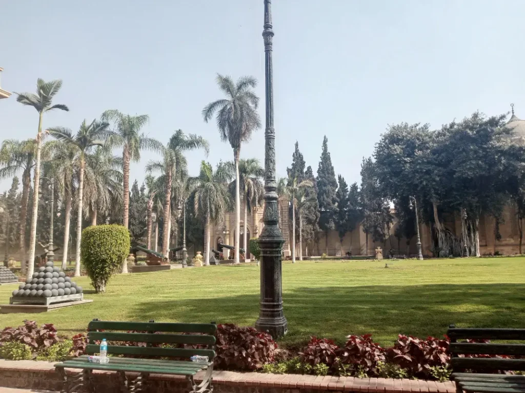 "حديقة متحف قصر عابدين الخضراء في قلب القاهرة، واحة تاريخية تضم أشجار نادرة، زهور ملونة، ونافورة موسيقية ساحرة بجوار القصر الملكي."